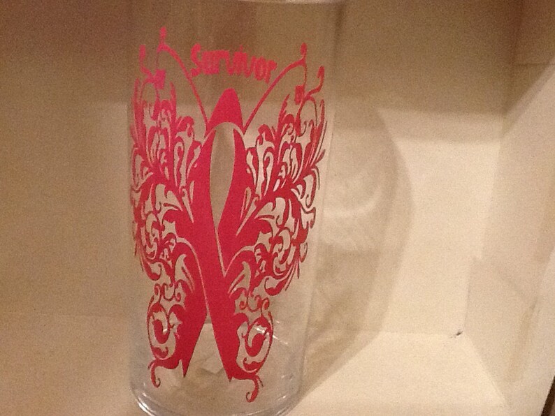 May include: A clear glass tumbler with a pink butterfly design and the word "Survivor" printed on the front.
