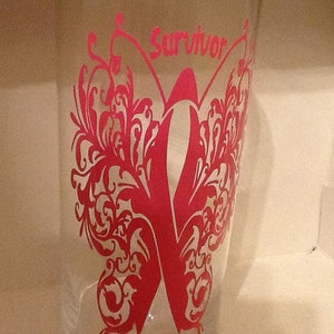 May include: A clear glass with a pink butterfly design and the word "Survivor" in pink lettering.