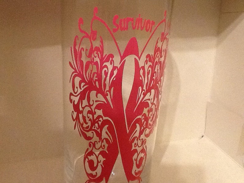 May include: A clear glass with a pink butterfly design and the word "Survivor" in pink lettering.