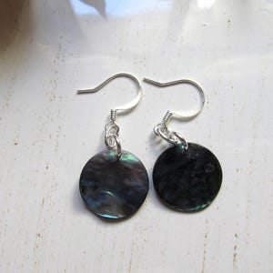 Peut inclure: Une paire de boucles d'oreilles en argent avec des pendentifs ronds en coquille noire et irisée.