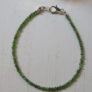 Puede incluir: Un delicado brazalete de piedras preciosas verdes con un cierre de plata.