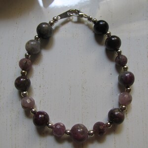 May include: A bracelet made of pink, gray, and black beads with silver accents. The bracelet has a silver clasp.