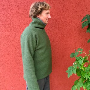 Puede incluir: Un su&eacute;ter verde de cuello alto con un cuello alto. El su&eacute;ter est&aacute; hecho de una tela suave y texturizada.