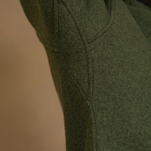 May include: Close-up of the green fabric of a jacket, showing the stitching detail of the seam.