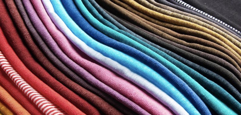 K&ouml;nnte beinhalten: Nahaufnahme einer Sammlung farbenfroher Stoffmuster, die diagonal angeordnet sind. Die Muster zeigen eine gro&szlig;e Auswahl an Farben, darunter Rot, Rosa, Blau, Gr&uuml;n und Braun. Der Stoff scheint ein weiches Strickmaterial zu sein.