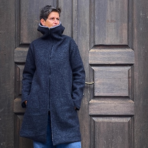 Puede incluir: Una chaqueta gris oscura con capucha y cierre de cremallera. La chaqueta tiene un cuello alto y está hecha de un tejido suave y texturizado.