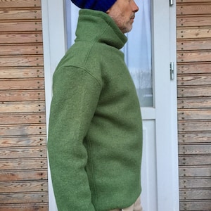 May include: A green turtleneck sweater with a high collar and long sleeves. The sweater is made of a soft, textured fabric. The person is wearing a blue beanie.