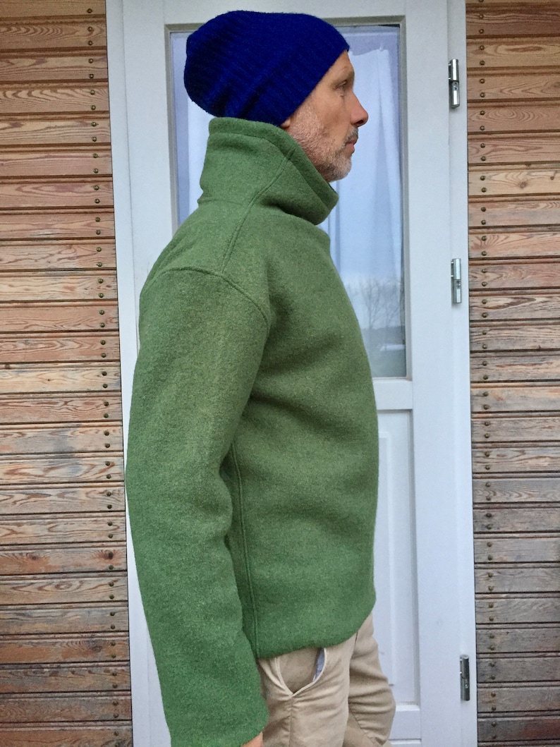 May include: A green turtleneck sweater with a high collar and long sleeves. The sweater is made of a soft, textured fabric. The person is wearing a blue beanie.