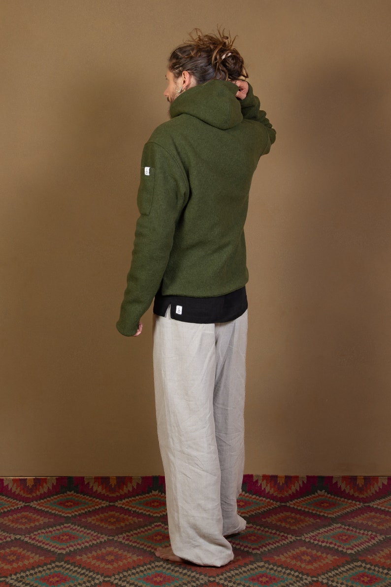 May include: A green hooded sweatshirt with a black undershirt and beige pants. The sweatshirt has a small white label on the left sleeve.