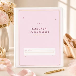 May include: A light pink binder titled DANCE MOM SEASON PLANNER with the subtitle SCHEDULE - SUPPORT - SHINE. The cover features small star icons, a white rectangular label area with the text DANCE MOM / FAN & 1, and a thin gold border.
