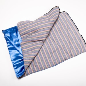 May include: A blue and pink striped blanket with a blue satin lining. The blanket is folded in half and has a black trim.