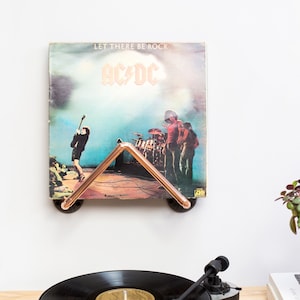 May include: A copper pipe record holder with a vinyl record of AC/DC's album "Let There Be Rock" displayed. The record holder is mounted on a white wall.