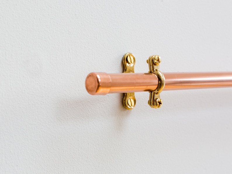 Wall mounted utensil rail made from polished copper, with solid brass fittings and screws. It is holding brass utensils and a pan using the solid copper hooks.