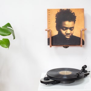 Vinyl record  holder that is wall mounted, ideal for holding up to 15 records. It is made from polished copper pipe, and allows you to flick through your records whilst still displaying the covers.