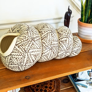 Op de afbeelding: Een witte keramische vaas met een bruin geometrisch patroon. De vaas is spiraalvormig en heeft een brede opening aan de bovenkant.