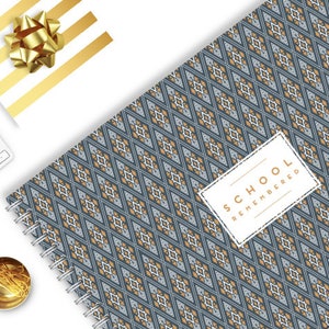 Op de afbeelding: Een blauw en gouden spiraalnotitieblok met een geometrisch patroon en de tekst "SCHOOL REMEMBERED" op een wit label.