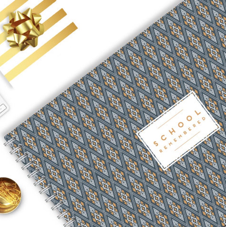 Op de afbeelding: Een blauw en gouden spiraalnotitieblok met een geometrisch patroon en de tekst "SCHOOL REMEMBERED" op een wit label.