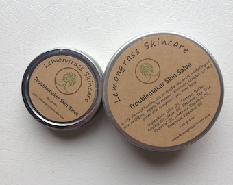 May include: Two silver tins of Lemongrass Skincare Troublemaker Skin Salve. The larger tin is 120 grams and the smaller tin is 30 grams. Both tins have a brown label with a green tree logo and the text "Lemongrass Skincare Troublemaker Skin Salve".