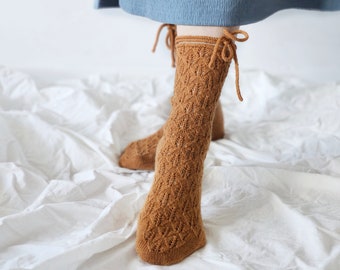 May include: A pair of brown lace-up socks with a delicate knit pattern. The socks are tied with a brown ribbon at the top.