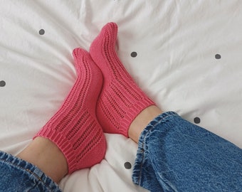 May include: A pair of pink knitted socks with a lacy pattern. The socks are worn by a person wearing blue jeans.