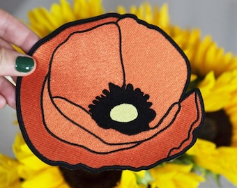 May include: A red felt poppy flower patch with black and yellow details. The patch is embroidered and has a slightly frayed edge.