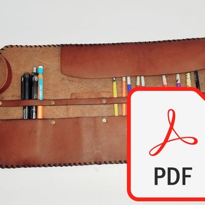 May include: A brown leather pencil roll with a flap closure. The roll is open and filled with colored pencils and pens. The roll has a stitched edge and metal snaps.