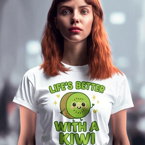 Könnte beinhalten: Ein weißes T-Shirt mit dem Text "LIFE'S BETTER WITH A KIWI" und einem Cartoon-Kiwi-Design. Die Kiwi ist grün und braun mit einem lächelnden Gesicht. Die Person auf dem Bild trägt ein weißes T-Shirt und eine schwarze Hose.