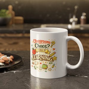 May include: A white ceramic mug featuring a colorful graphic design with the text "Classroom Chaos? I CALL IT LEARNING". The illustration includes a red apple, a yellow pencil, a green notebook, a yellow star, and various small school-themed icons.