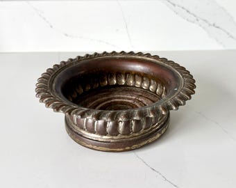 May include: A detailed, antique-style metal bowl with a decorative, ridged rim. The bowl has a dark, aged appearance with a circular base and a detailed, textured design. The color is a mix of bronze and silver.