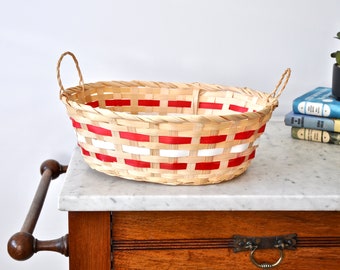 May include: A woven oval basket with red and white stripes. The basket has two handles and is sitting on a marble surface.