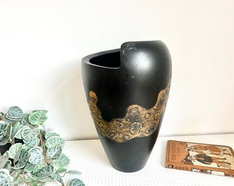 May include: Black ceramic vase with a gold abstract design. The vase has a wide opening and a rounded bottom.