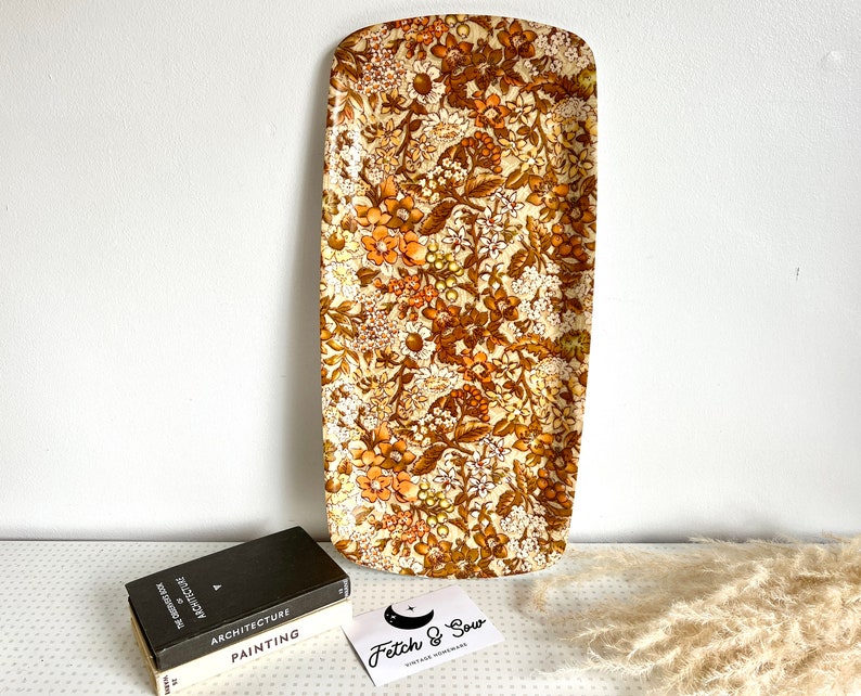 May include: A vintage rectangular serving tray with a floral pattern in shades of brown, orange, and white. The tray is made of plastic and has a glossy finish.