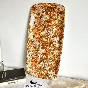 May include: A vintage rectangular serving tray with a floral pattern in shades of brown, orange, and white. The tray is made of a hard plastic material.