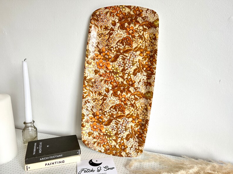 May include: A vintage rectangular serving tray with a floral pattern in shades of brown, orange, and white. The tray is made of a hard plastic material.