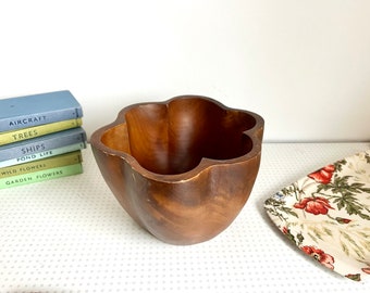 May include: A brown wooden bowl with a five-pointed star shape. The bowl is sitting on a white surface with a floral pattern.