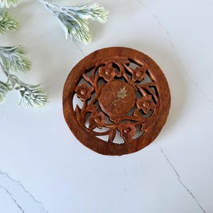 May include: A round wooden coaster featuring intricate floral carvings and a gold inlay in the centre.