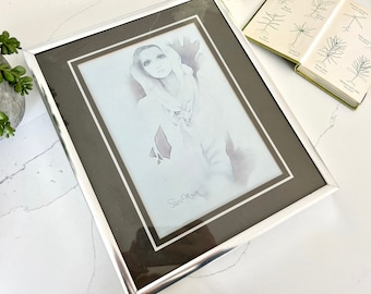 May include: A framed black and white drawing of a woman with long hair wearing a scarf. The drawing is signed "Sam Osborn" in the bottom right corner.