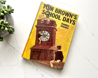 May include: A yellow book cover with a brown clock tower and two figures. The book title is "Tom Brown's School Days" by Thomas Hughes.