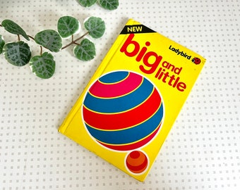 May include: A yellow children's book with the title "big and little" in red and black text. The book is from the Ladybird series and features a red, blue, and pink striped ball on the cover.