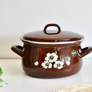 May include: Brown enamel pot with a white floral design and a silver lid. The pot has two handles and a silver rim.