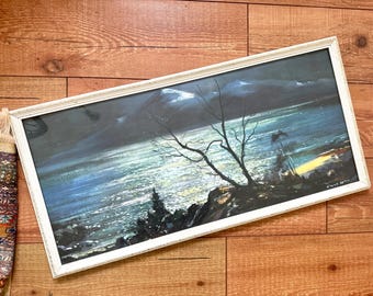 May include: An original landscape painting in a white distressed frame. The artwork depicts a moonlit seascape with a silhouetted tree in the foreground. The painting features shades of blue, black, and white, creating a serene and atmospheric scene.