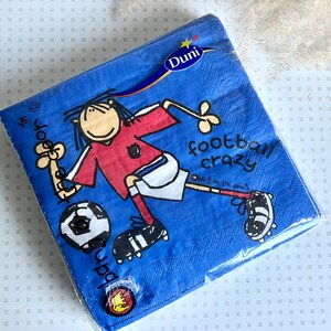 May include: Blue paper napkins with a cartoon illustration of a soccer player kicking a ball. The text "Football Crazy" is printed on the napkins. The napkins are packaged in a clear plastic bag.