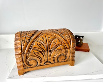 May include: A wooden box with intricate carvings of leaves and flowers. The box is a light brown color and has a rounded top.