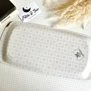 May include: A white metal serving tray with a delicate floral pattern. The tray has a slightly rounded shape and a raised edge. The bottom of the tray has a small black and white sticker with a butterfly design.