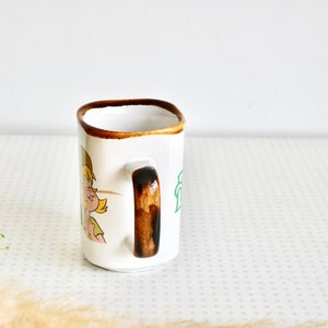 K&ouml;nnte beinhalten: Wei&szlig;e Keramiktasse mit braunem Henkel und einer Comic-Illustration eines M&auml;dchens mit blonden Haaren. Die Tasse hat einen braunen Rand und eine gr&uuml;ne Aufschrift.