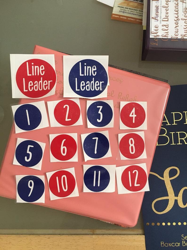 May include: A pink binder with blue and red circular stickers. The stickers have numbers 1 through 12 and the words "Line Leader" on two of the stickers.