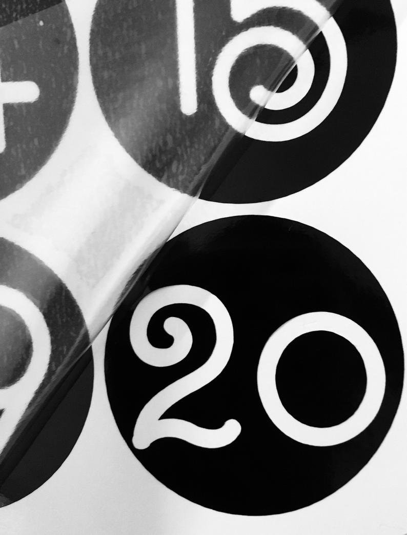 May include: Black and white circular stickers with the numbers 15 and 20 printed in white. The stickers are on a white background.