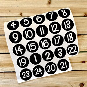 May include: A set of 24 black and white round stickers with numbers 1 through 24 printed in white on a black background.