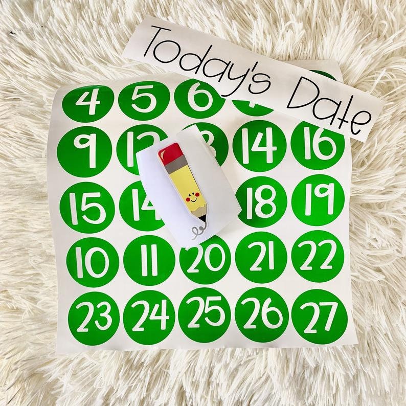 May include: A set of green circle stickers with white numbers 4 through 27. The stickers are arranged in a grid pattern on a white sheet of paper. A white card with the text "Today's Date" is on top of the stickers. A small pencil sticker is on top of the card.