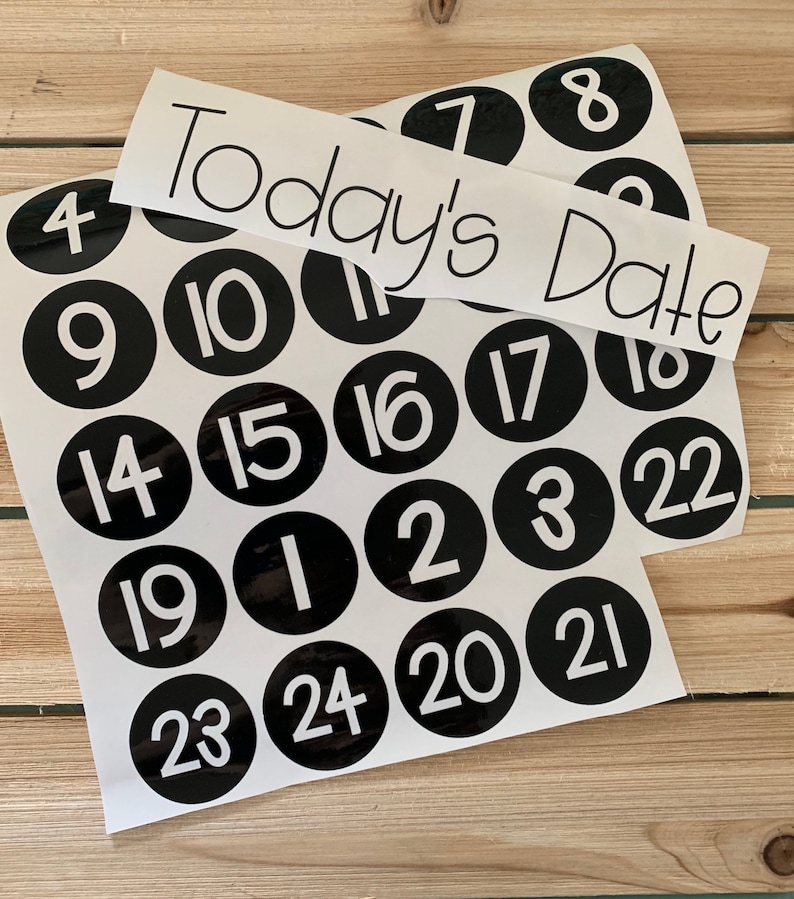 May include: A set of black and white circular stickers with numbers 1 through 24. The stickers are arranged in a grid pattern. A white banner with the text "Today's Date" is placed on top of the stickers.